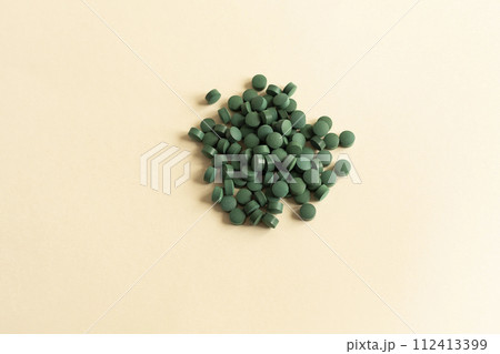 Flat Lay Vitamin, Easy To Swallow Green Pills Of Natural Spirulina On Beige Background. They Are Made Of Blue-green Algae With Strong Antioxidant Effects. Horizontal. Flat Lay Vitamin, Easy To Swallow Green Pills Of Natural Spirulina On Beige Background. They Are Made Of Blue-green Algae With Strong Antioxidant Effects. Horizontal. 112413399