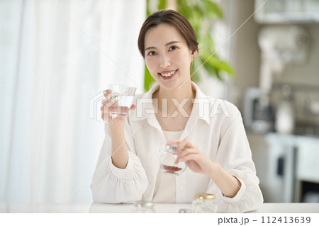 リビングでサプリメントを飲む女性 112413639