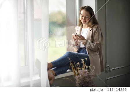 Work-life-balance, businesswoman on the windowsill in the office with smartphone Work-life-balance, businesswoman on the windowsill in the office with smartphone 112414825