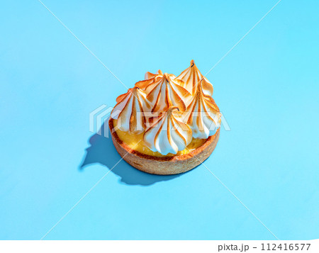Mini cake decorated with whipped egg whites meringue. Mini lemon tart with burnt French meringue. Delicious dessert with lemon filling. topped with meringue on blue background, hard shadows copy space 112416577