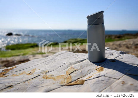【南知多】海岸の岩場に置かれたグレーの水筒 112420329