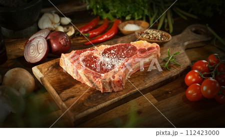 A view of a fresh raw beef steak on a wooden board placed on the kitchen counter. The concept of meat preparation. A view of a fresh raw beef steak on a wooden board placed on the kitchen counter. The concept of meat preparation. 112423000