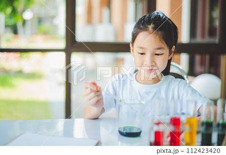 little scientist looking through a microscope and test tubes filled with chemicals for learning about science and experiments. 112423420