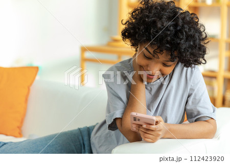 African girl holding smartphone touch screen typing scroll page at home. Woman with cell phone surfing internet using social media apps playing game. Shopping online Internet news cellphone addiction African girl holding smartphone touch screen typing scroll page at home. Woman with cell phone surfing internet using social media apps playing game. Shopping online Internet news cellphone addiction 112423920