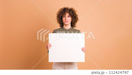 Happy woman holding blank paper in beige studio Happy woman holding blank paper in beige studio 112424797