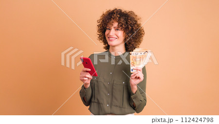 Excited woman with cash and looking phone in beige studio Excited woman with cash and looking phone in beige studio 112424798