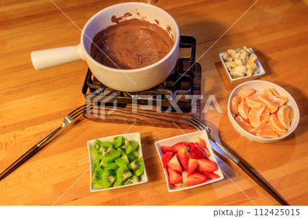 Chocolate fondue with fruits on wooden table. Cooking fondue Chocolate fondue with fruits on wooden table. Cooking fondue 112425015