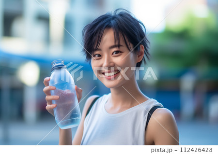 笑顔の若い女性が水のボトルを持ってポーズをとる 112426428