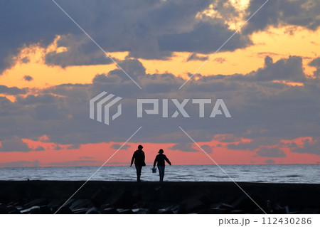 夕暮れ時に海岸を歩く人 夕暮れ時に海岸を歩く人 112430286