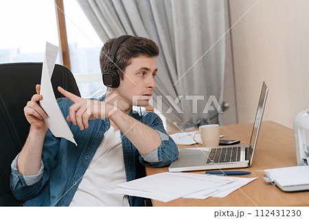 Serious handsome guy works remotely using laptop for video call 112431230