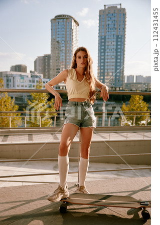 Cool hipster woman skateboarder posing with her longboard over cityscape 112431455