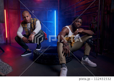 Two young drug dealers with serious faces posing for camera in neon light Two young drug dealers with serious faces posing for camera in neon light 112431532