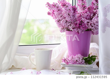 The postcard is beautiful. A mug of tea, an old book and a bouquet of purple lilac. A beautiful still life. Spring time. The concept of Good morning. The postcard is beautiful. A mug of tea, an old book and a bouquet of purple lilac. A beautiful still life. Spring time. The concept of Good morning. 112431595