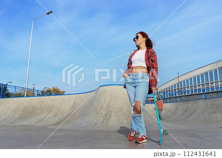 An active middle-aged woman rides a skateboard on an empty road or highway. An ordinary city woman relaxing on a skateboard after work. The concept of a modern lifestyle An active middle-aged woman rides a skateboard on an empty road or highway. An ordinary city woman relaxing on a skateboard after work. The concept of a modern lifestyle 112431641