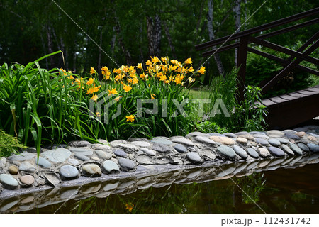 A cozy garden with a decorative lake and a bridge in summer. A cozy garden with a decorative lake and a bridge in summer. 112431742