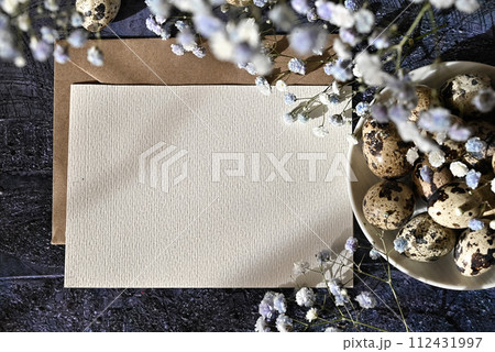 Create an Easter composition of Easter quail eggs and flowers on a white wooden background. A greeting card for the Easter holiday.Top view, copy location, flat layout. 112431997