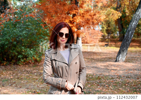a confident young slender woman in a raincoat and high-heeled shoes is talking on the phone in an autumn city, a woman is smiling and enjoying life 112432007