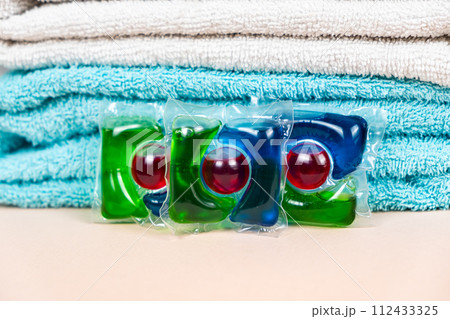 Laundry pods capsules on beige background with soft towels 112433325
