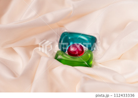 Liquid detergent gel in capsule on fabric close-up, space for text Liquid detergent gel in capsule on fabric close-up, space for text 112433336