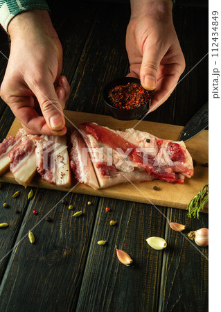 A man seasones lard with spices on a wooden cutting board. The concept of preparing delicious peasant lard with garlic for an appetizer 112434849