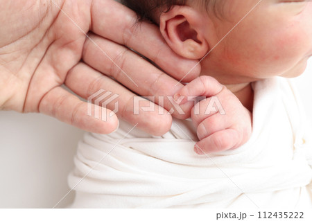 Close-up of baby's small hand, head, ear and palm of mother. Macro Photo of Newborn baby after birth tightly holding parents finger on white background. Family and home concept. Healthcare paediatrics 112435222