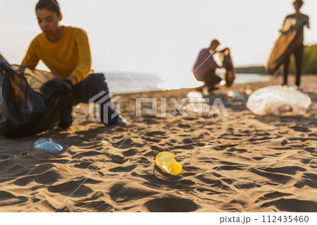 Earth day. Volunteers activists collects garbage cleaning of beach coastal zone. Woman mans with trash in garbage bag on ocean shore. Environmental conservation coastal zone cleaning. Blurred image 112435460