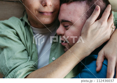 Portrait of young man with Down syndrome with his mother at home, holding, touching with foreheads. Concept of love and parenting disabled child. Close up. 112436037