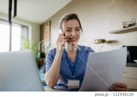Nurse paying bills online, working on notebook. Doctor working from home, after workday, telemedicine consultation. Work-life balance for healthcare worker. 112436120
