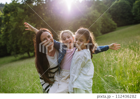 Beautiful mother with two daughters, playing at meadow, laughing, having fun. Concept of Mother's Day, maternal love. 112436282