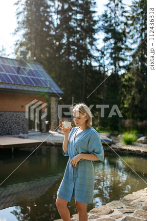 Young woman in bathrobe, checking temperature, ready for home spa procedure in hot tub outdoors. Wellness, body care, hygiene concept. 112436318