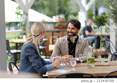 Couple sitting outdoors on terrace restaurant, having dinner date. Business lunch for two managers, discussing new business project. Couple sitting outdoors on terrace restaurant, having dinner date. Business lunch for two managers, discussing new business project. 112436708