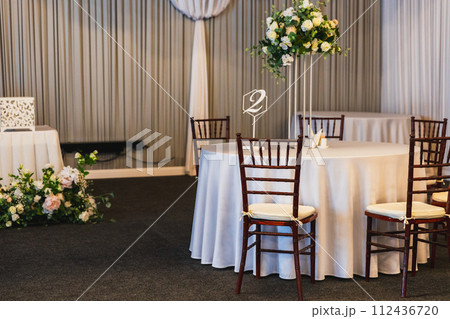 Decorated interior for festive event. Fancy table set for dinner with flower composition in restaurant, luxury interior background. Wedding elegant banquet decoration arranged by catering service Decorated interior for festive event. Fancy table set for dinner with flower composition in restaurant, luxury interior background. Wedding elegant banquet decoration arranged by catering service 112436720