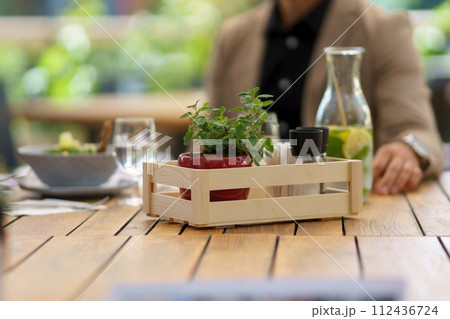 Wooden table on restaurant patio. Dining table with salt, spices, seasoning containers in crate, small plant as decoration. Wooden table on restaurant patio. Dining table with salt, spices, seasoning containers in crate, small plant as decoration. 112436724