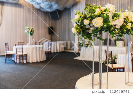 Decorated interior for festive event. Fancy table set for dinner with flower composition in restaurant, luxury interior background. Wedding elegant banquet decoration arranged by catering service 112436741