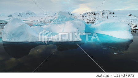 Global warming, melting icebergs in Antarctica. Glacier with melted cavity floating in blue ocean water. Polar climate change at sunny winter day. Cinematic ecology scene. Close up shot 112437972