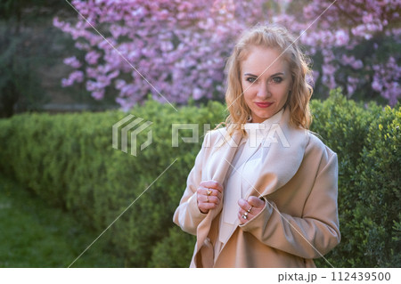 Attractive woman with red hair stare in camera in blooming spring park on cherry blossom tree background. Portrait. 112439500