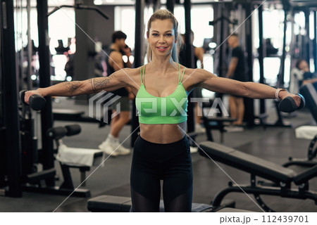 Muscular fitness woman athlete doing heavy weight exercise for shoulders with dumbbells in the gym Muscular fitness woman athlete doing heavy weight exercise for shoulders with dumbbells in the gym 112439701