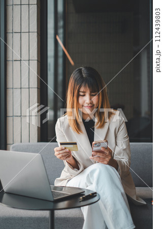 Mobile Shopping. Cheerful woman using smartphone shopping online holding credit card making payment sitting on sofa at home. Internet banking application and e-commerce. Mobile Shopping. Cheerful woman using smartphone shopping online holding credit card making payment sitting on sofa at home. Internet banking application and e-commerce. 112439803