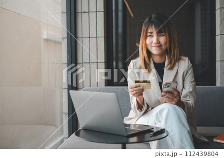 Mobile Shopping. Cheerful woman using smartphone shopping online holding credit card making payment sitting on sofa at home. Internet banking application and e-commerce. 112439804