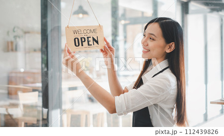 Young entrepreneur holding open sign on glass door at cafe Young entrepreneur holding open sign on glass door at cafe 112439826