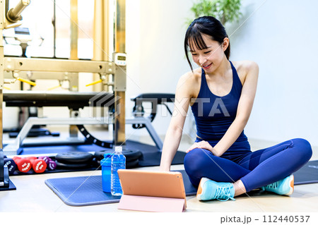 パーソナルジムで体を鍛える若い笑顔の女性 タブレットで動画視聴 鍛える方法を調べる くっきり寒色西日 パーソナルジムで体を鍛える若い笑顔の女性 タブレットで動画視聴 鍛える方法を調べる くっきり寒色西日 112440537