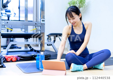 パーソナルジムで体を鍛える若い笑顔の女性 タブレットで動画視聴 鍛える方法を調べる 寒色 パーソナルジムで体を鍛える若い笑顔の女性 タブレットで動画視聴 鍛える方法を調べる 寒色 112440538