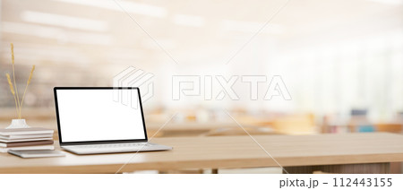A laptop computer mockup and books on a wooden table in a reading room in a library or classroom. 112443155