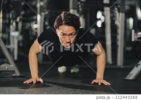 トレーニングジムで真剣な表情で腕立て伏せをするストイックな若い男性 トレーニングジムで真剣な表情で腕立て伏せをするストイックな若い男性 112443268