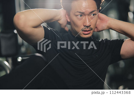 トレーニングジムで真剣な表情で腹筋をするストイックな若い男性 112443368