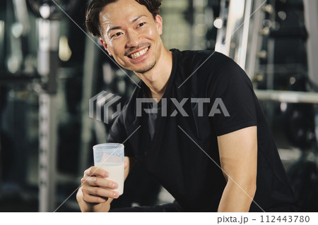 トレーニングジムでプロテインを飲む若い男性 112443780