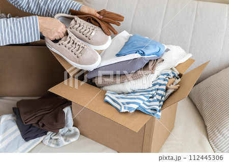 Donation concept. A woman puts clothes in a box at home for donation, recycling or disposal. 112445306