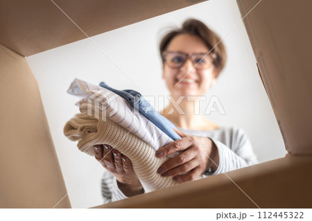 Donation concept. A woman puts clothes in a cardboard box at home for donation, recycling  112445322