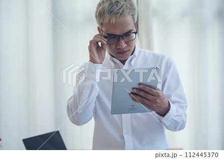 Asian Man thinking wear eyeglasses using laptop at home office. Desperate man stress headache depressed from startup small business at home office. Failure businesman working holding smart tablet Asian Man thinking wear eyeglasses using laptop at home office. Desperate man stress headache depressed from startup small business at home office. Failure businesman working holding smart tablet 112445370