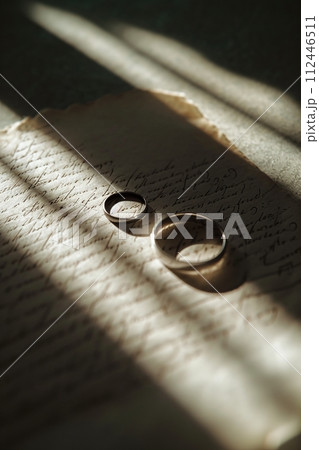 Wedding rings on a letter in dramatic light. AI Generated. 112446511